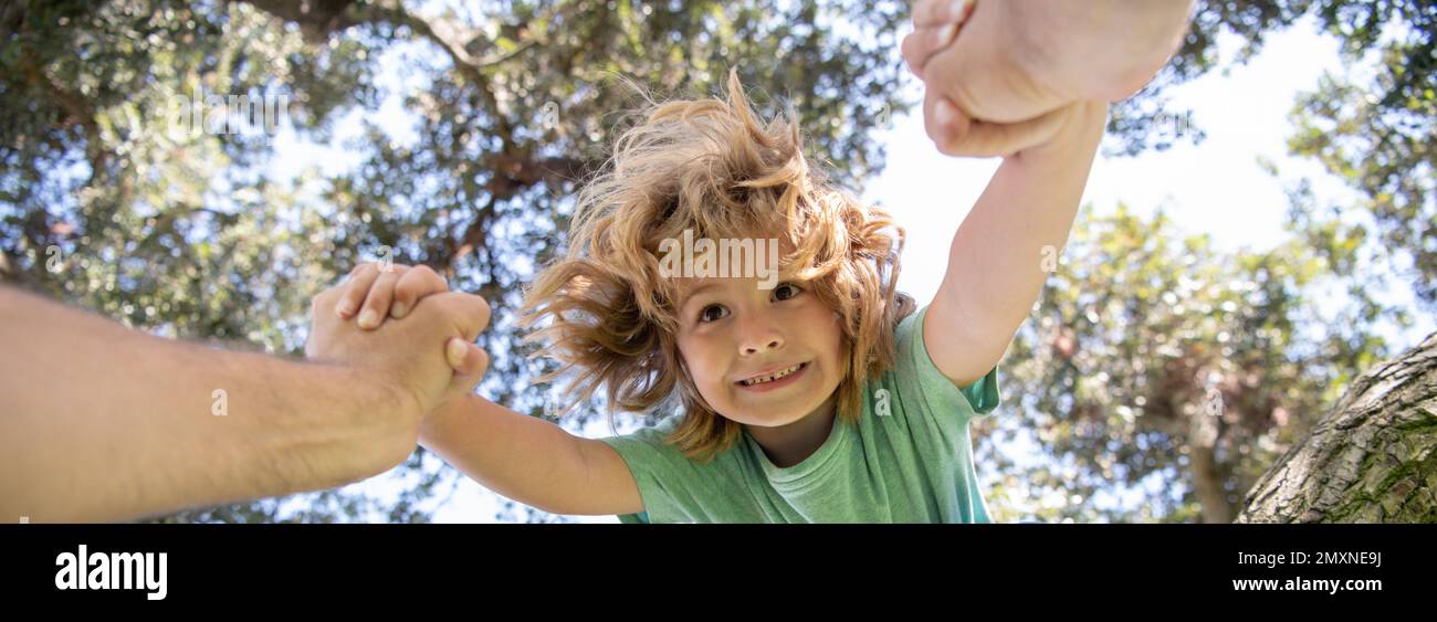 Fathers hand. A father helping his son down from the branch of a tree. Spring banner. Stock Photo