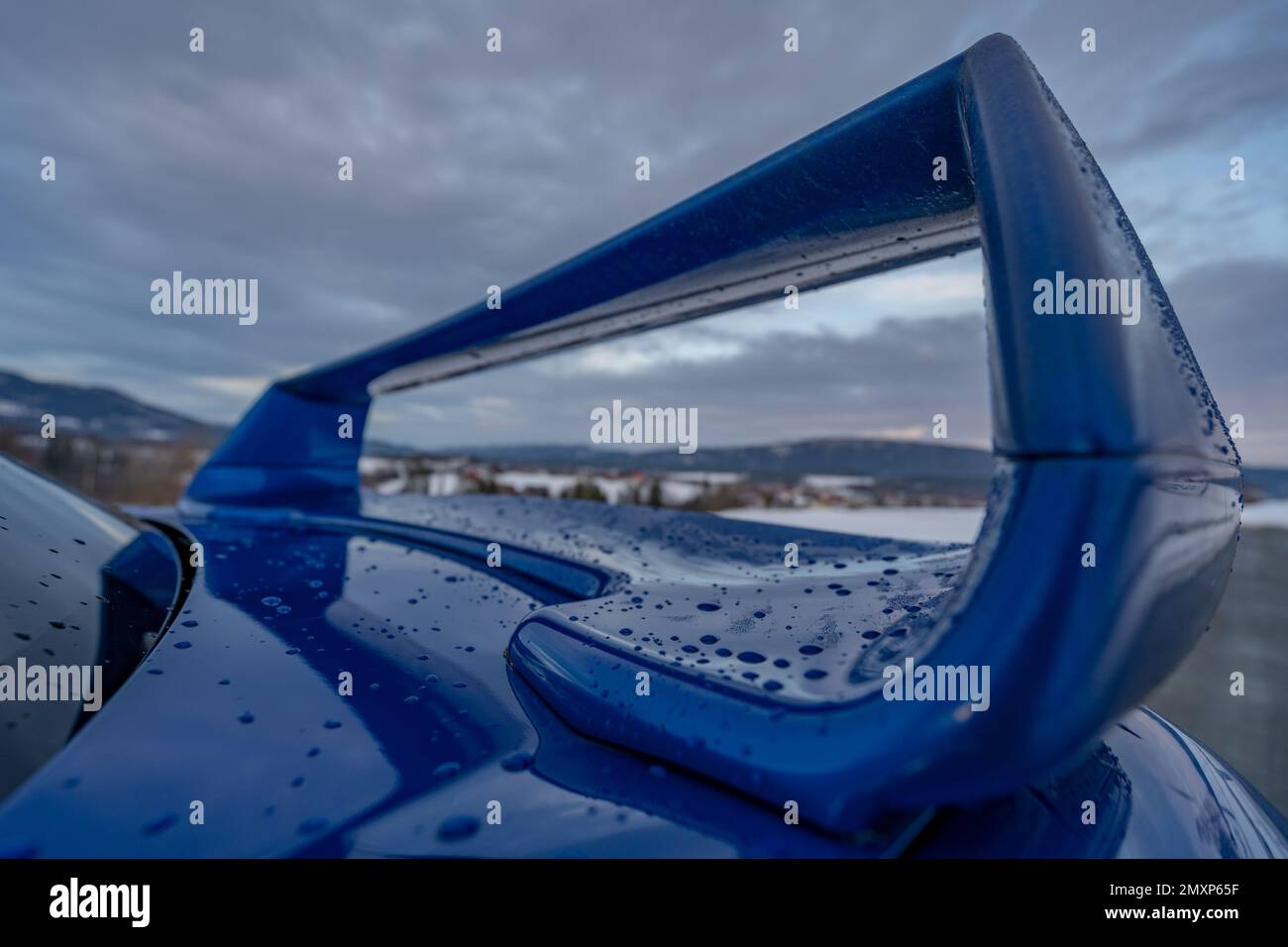 A closeup of a blue car wing with raindrops against the background of the cloudy sky. Stock Photo