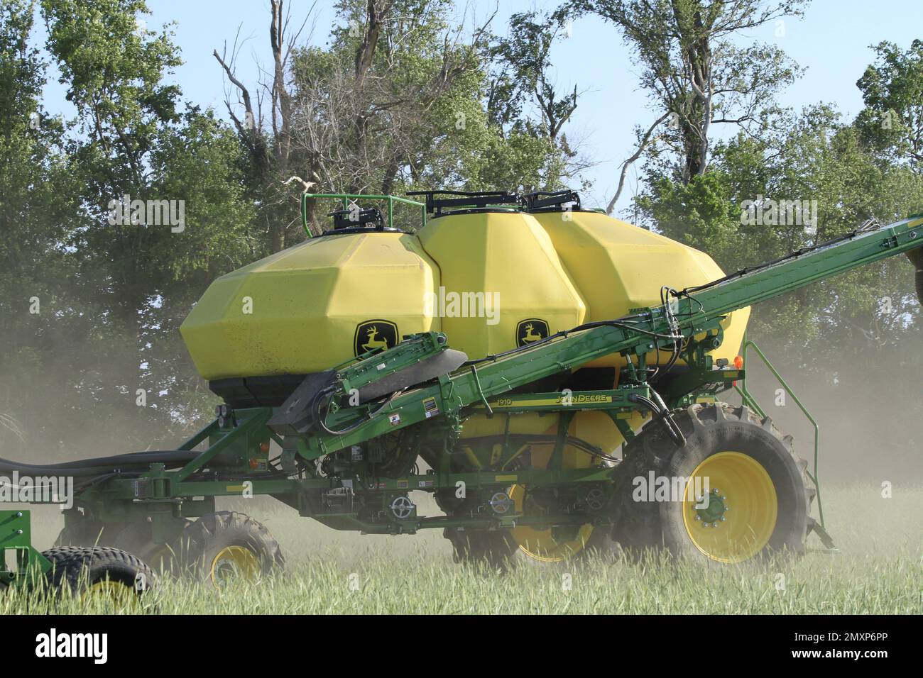 A John Deere Sprayer in a farm field with trees and sky Stock Photo