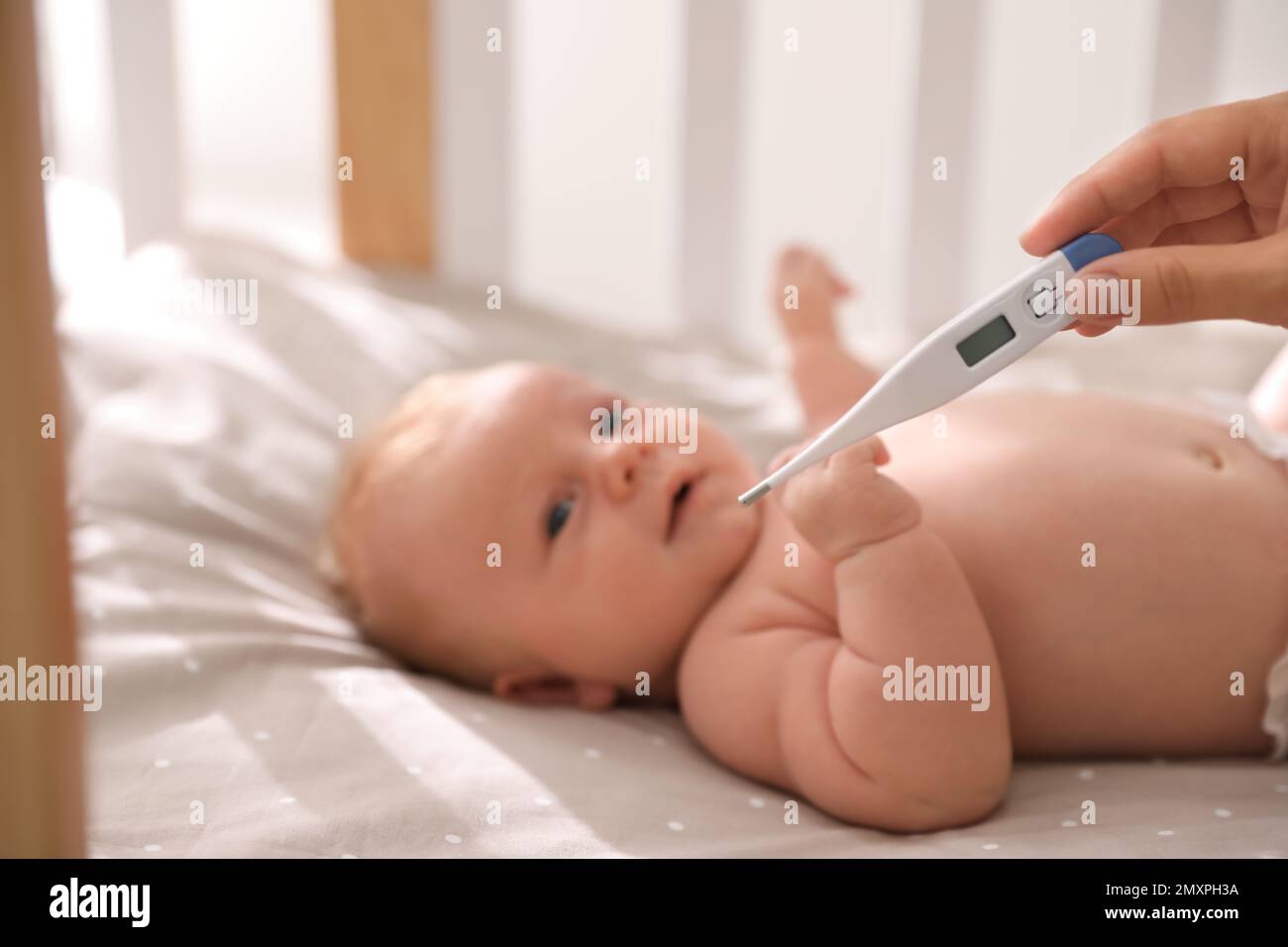 https://c8.alamy.com/comp/2MXPH3A/cute-baby-lying-in-crib-focus-on-woman-holding-digital-thermometer-health-care-2MXPH3A.jpg