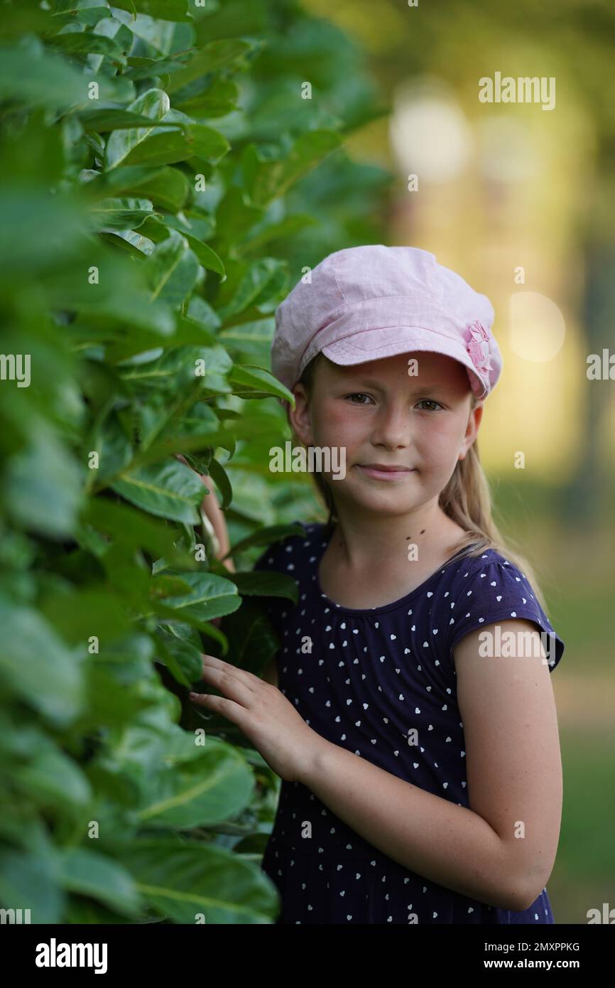 Cute caucasian little girl in a pink hat standing near the blooming ...