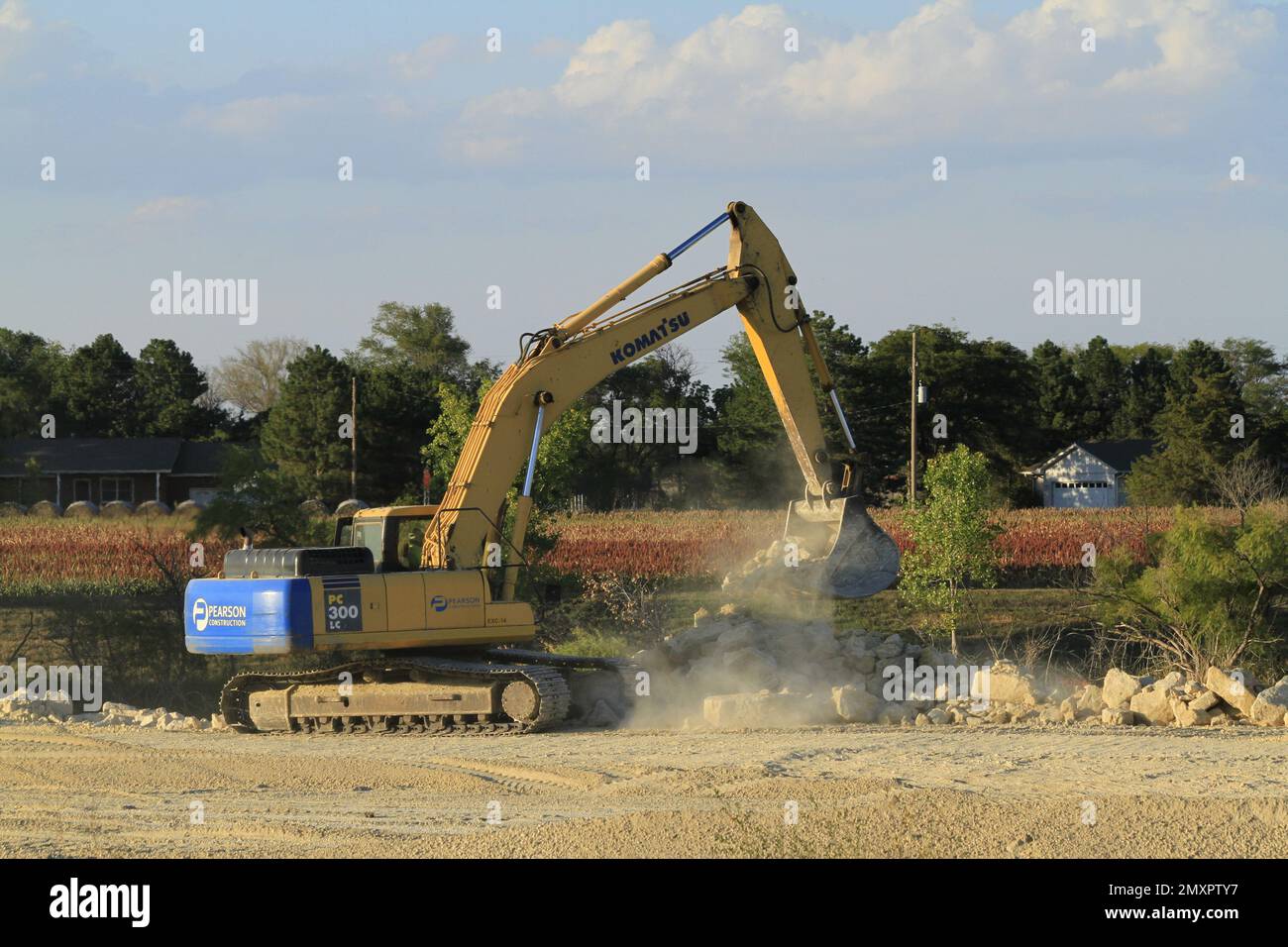 A KAMATSU EXCAVATOR moving rocks with tree's and blue sky at a construction site Stock Photo