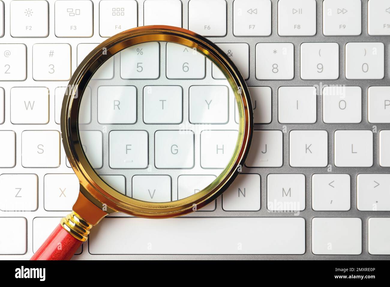 Magnifier glass on modern keyboard, top view. Find keywords concept