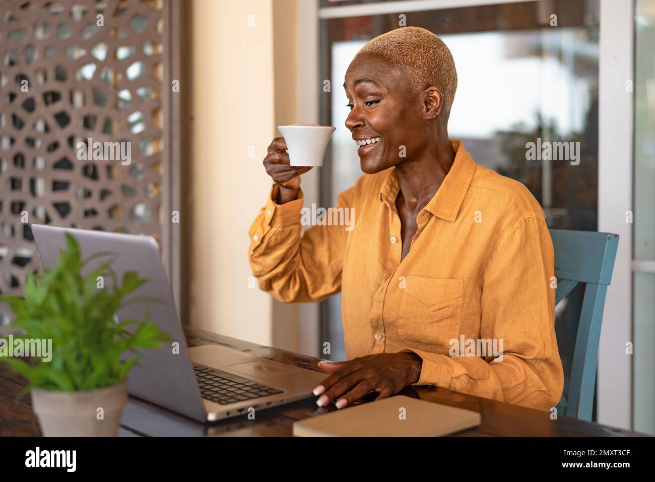 Happy African woman drinking a coffee while working with laptop at the