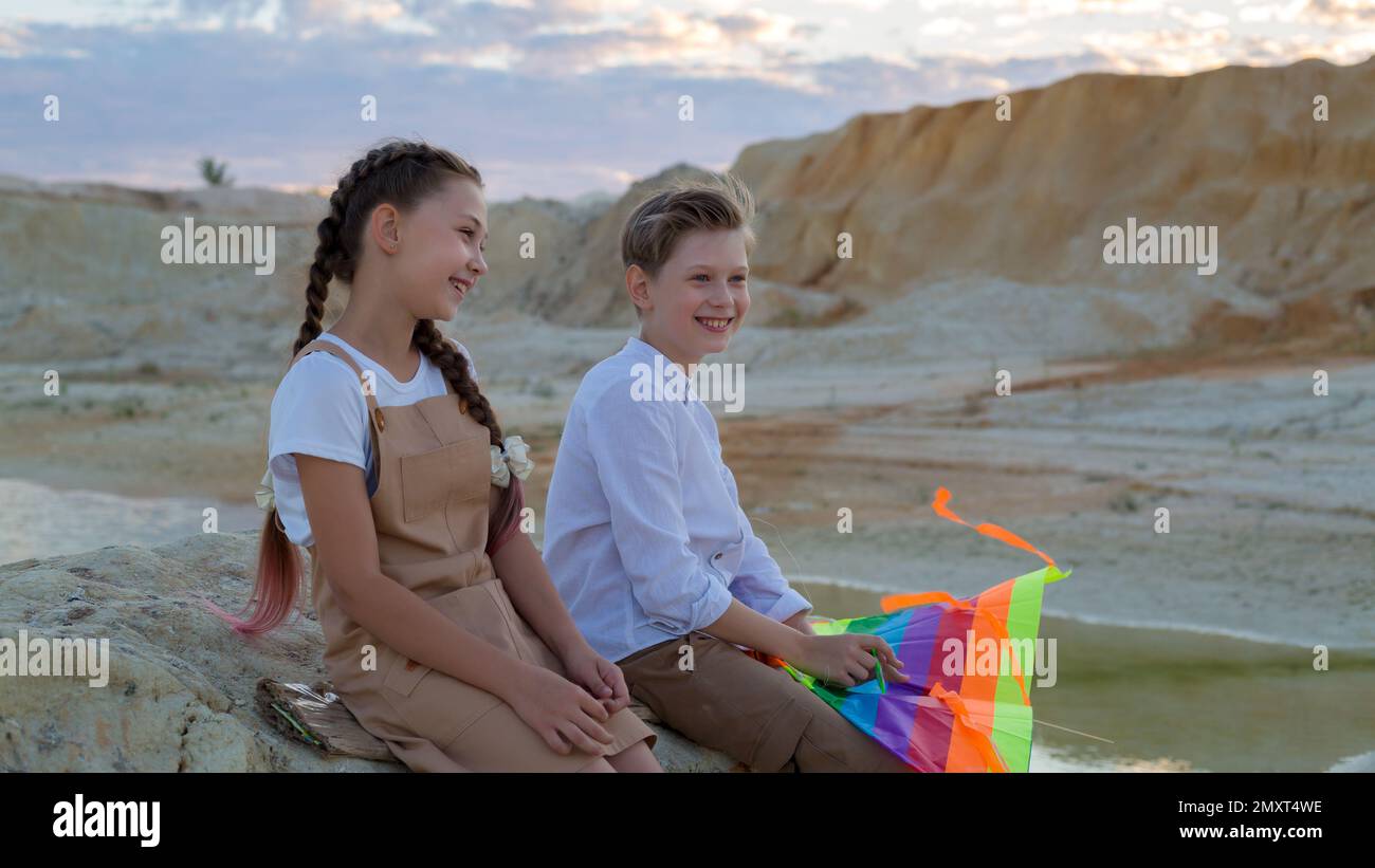 A boy and a girl 8-9 years old with a kite are having fun talking on the mountain. Stock Photo