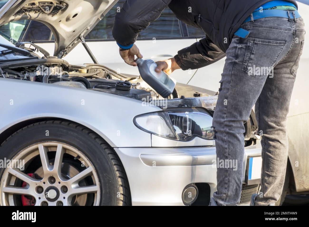 A car with the hood up and a man pouring motor oil into the engine Stock Photo Alamy