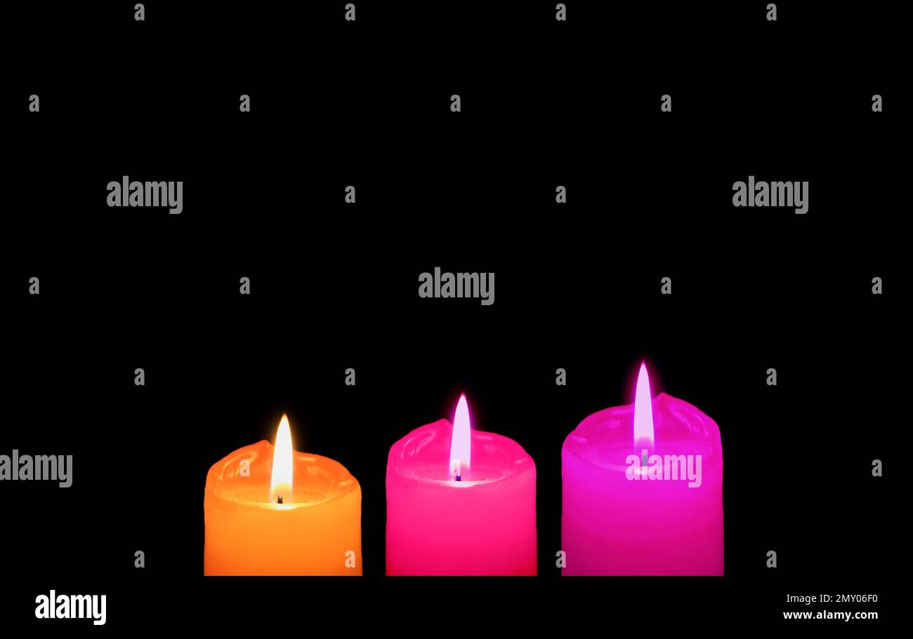 Burning Three of Different Vibrant Colors Candles on Black Backdrop with Copy Space Stock Photo