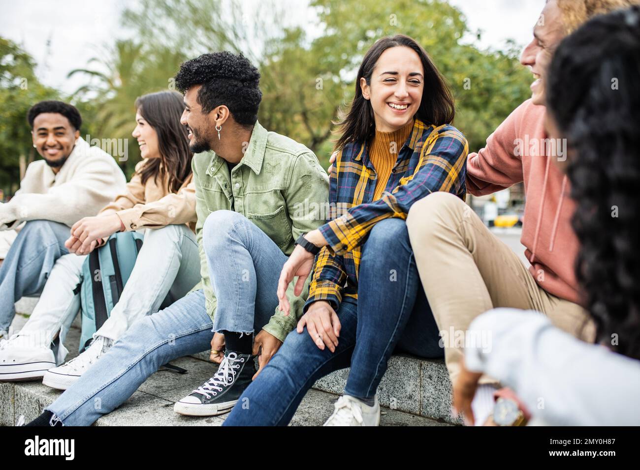 Multi-ethnic young group of united friends laughing while sitting outdoors Stock Photo