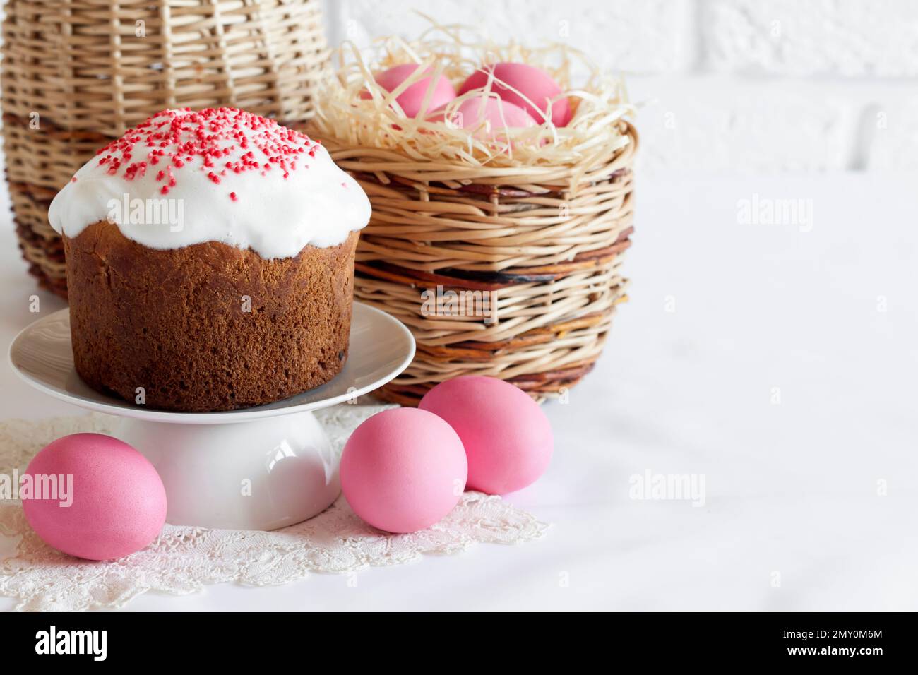 Minimalistic Easter composition with wicker basket with pink colored eggs and Easter cake on white background. Copy space Stock Photo