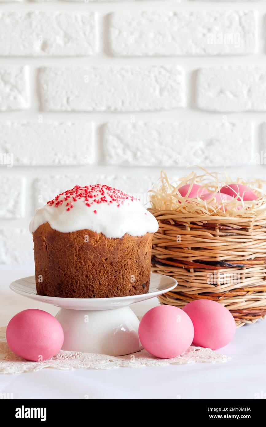 Minimalistic Easter composition with wicker basket with pink colored eggs and Easter cake on white background. Copy space Stock Photo