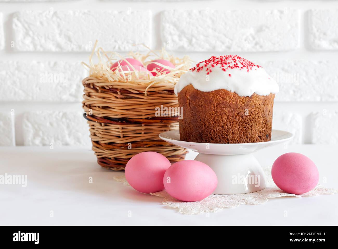 Minimalistic Easter composition with wicker basket with pink colored eggs and Easter cake on white background Stock Photo
