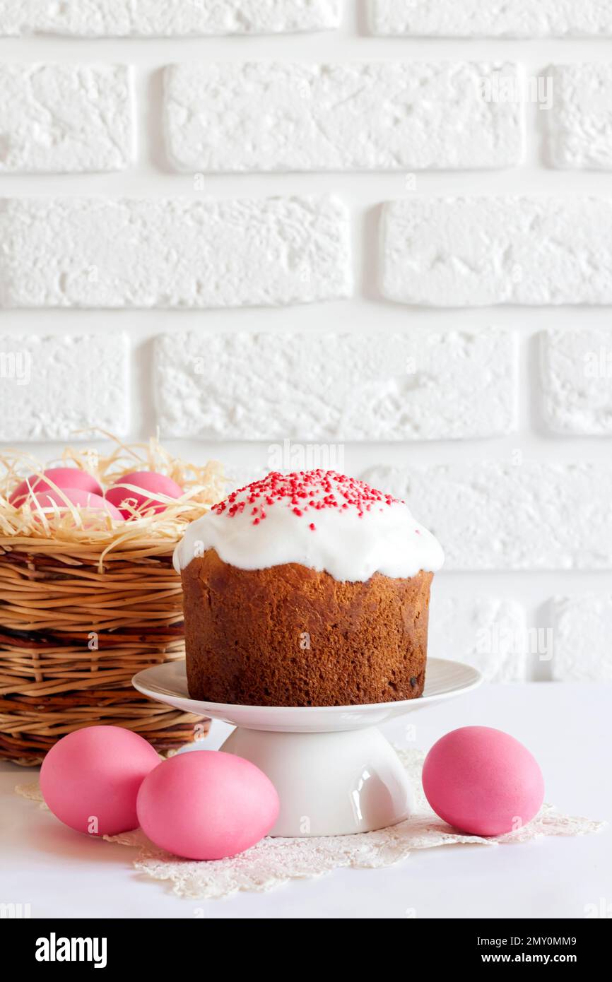 Minimalistic Easter composition with wicker basket with pink colored eggs and Easter cake on white background. Copy space Stock Photo