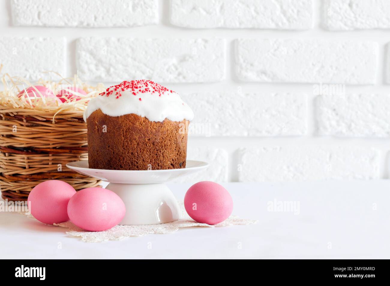 Minimalistic Easter composition with wicker basket with pink colored eggs and Easter cake on white background. Copy space Stock Photo