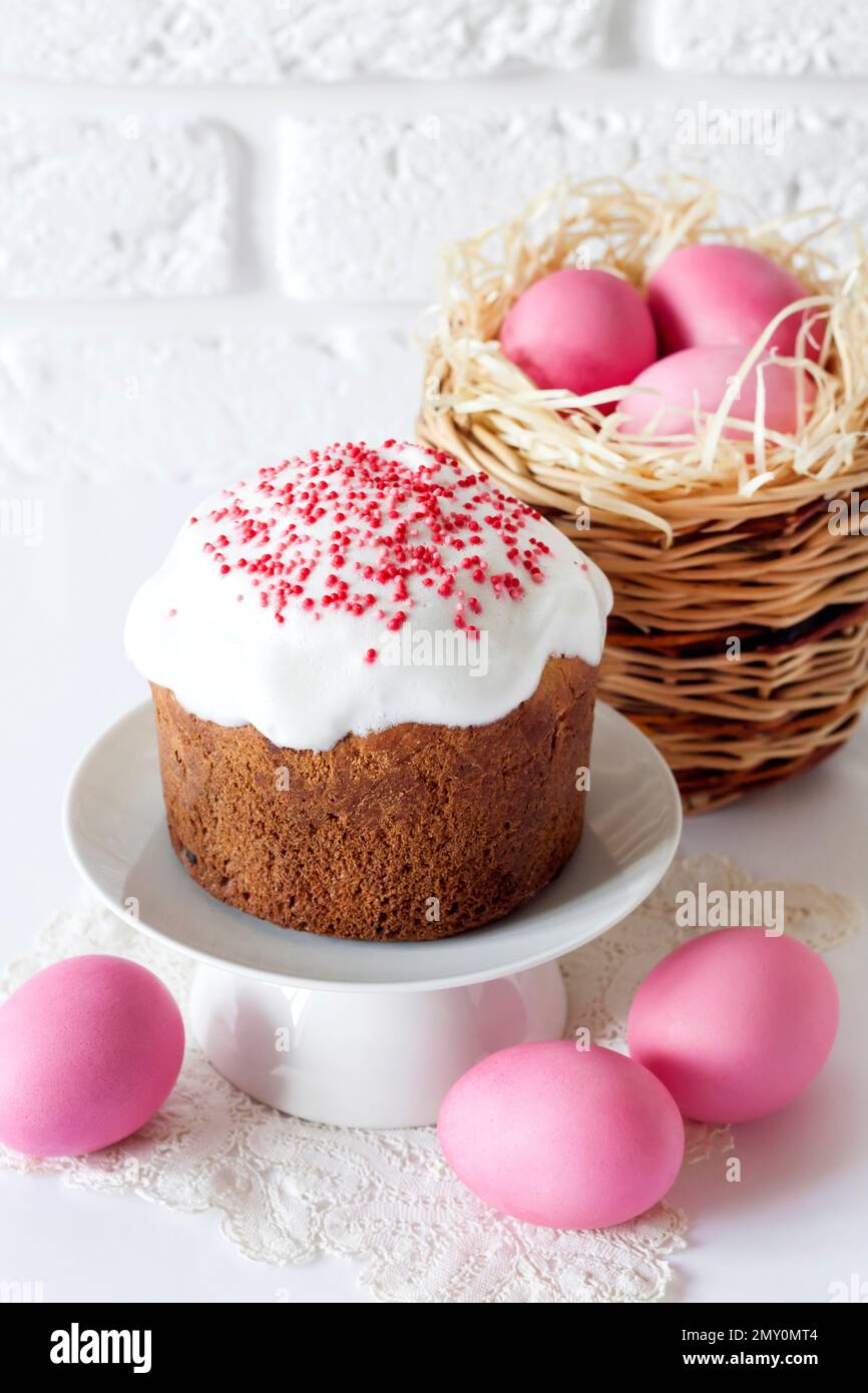 Minimalistic Easter composition with wicker basket with pink colored eggs and Easter cake on white background Stock Photo