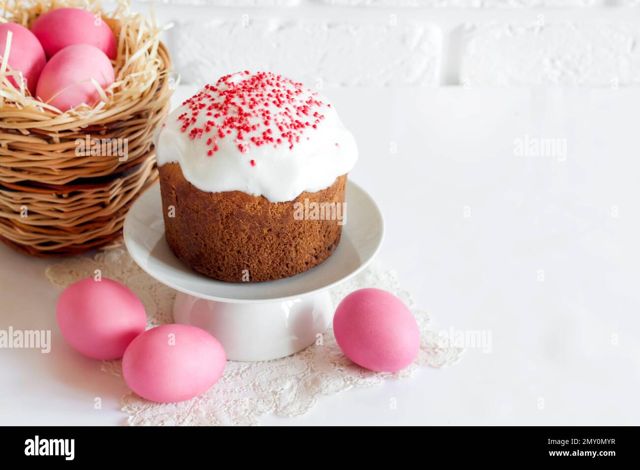 Minimalistic Easter composition with wicker basket with pink colored eggs and Easter cake on white background. Copy space Stock Photo