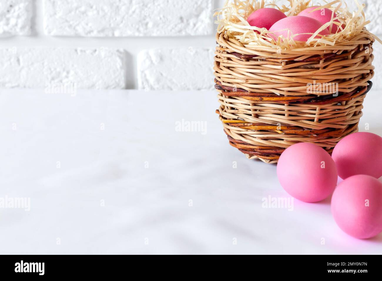 Minimalistic Easter composition with wicker basket and pink colored eggs on white background. Copy space Stock Photo