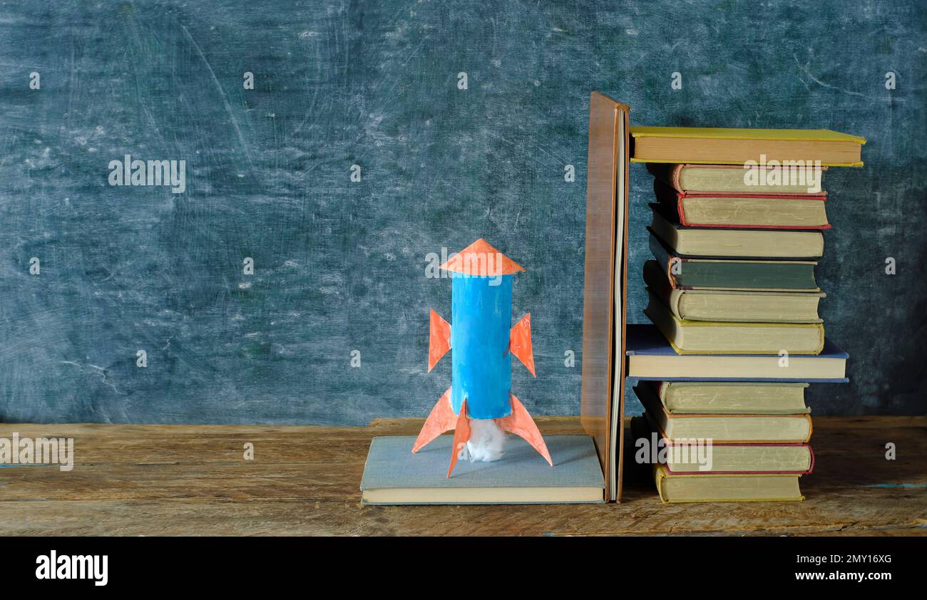 Stack of hardback books with rocketship launching on blackboard background.Learning,education is power,personal development, ladder of sucess and back Stock Photo
