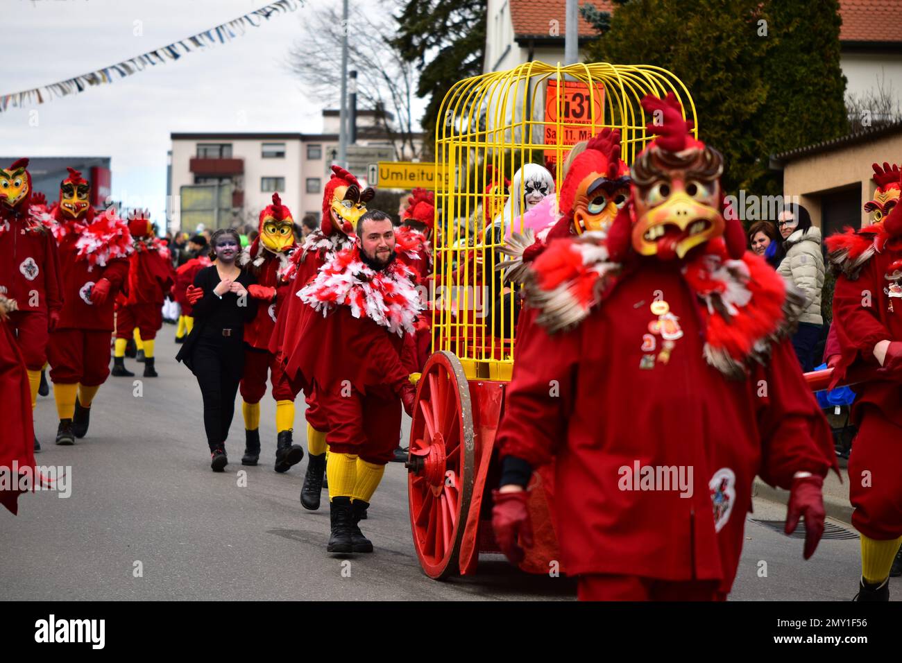 A German Carnival ceremony in the streets of Neuhausen with people in red rooster costumes and caged prisoners parading Stock Photo