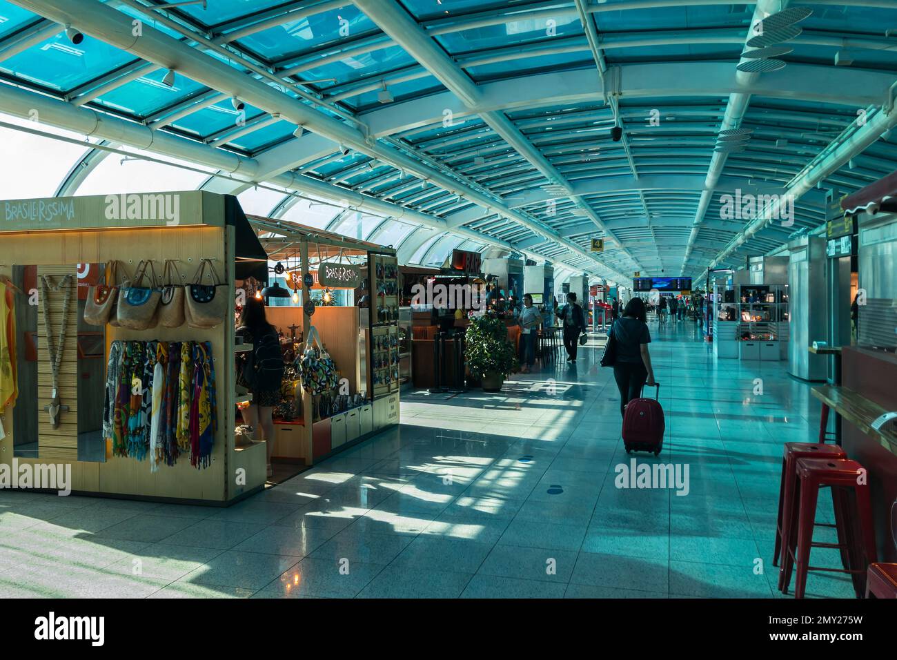 Small kiosk stores selling products located inside the populated Santos Dumont airport departure room passenger terminal in early summer morning. Stock Photo