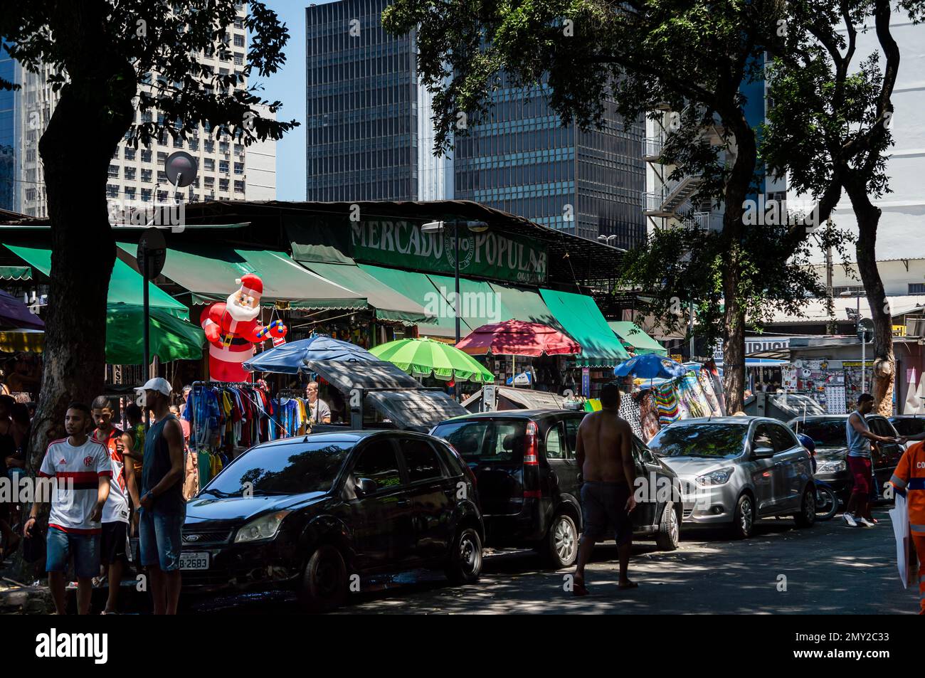 The entrance of Uruguaiana popular market with lots of umbrellas and cars parked at it in Centro district under tree shade in a summer sunny day. Stock Photo