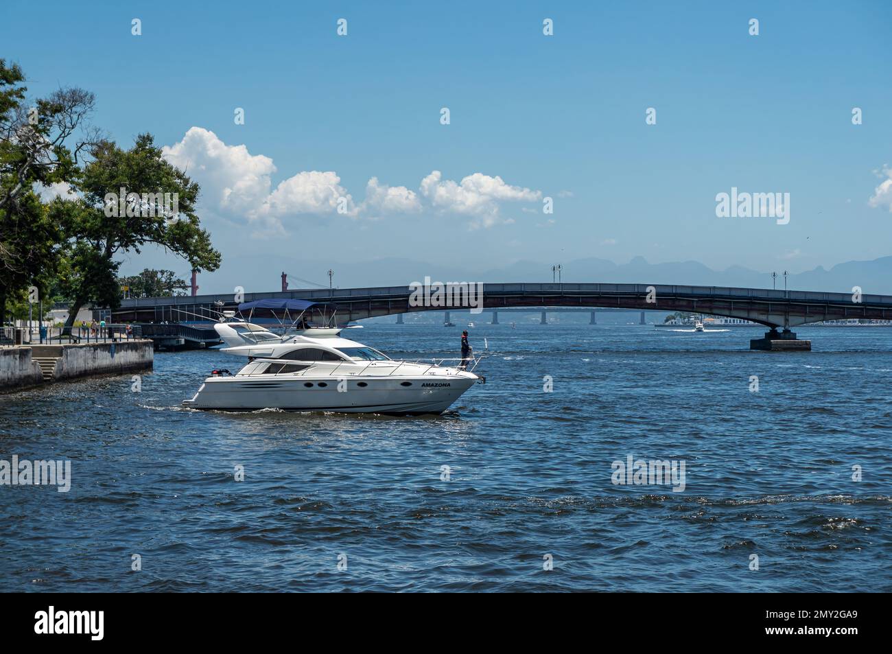 A white speedboat sailing on the blue waters of Guanabara bay, nearby Sao Bento Pier and Arnaldo Luz bridge under summer afternoon clear blue sky. Stock Photo