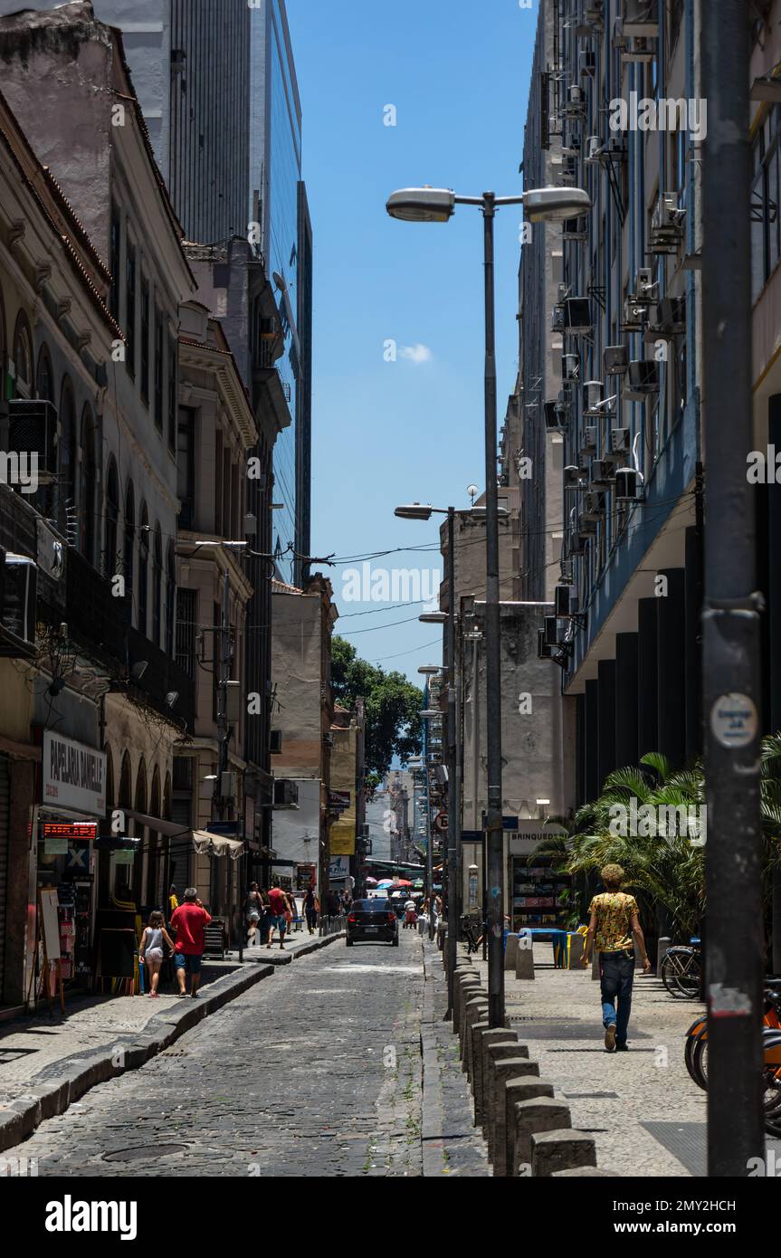 View of the narrow and populated Alfandega cobblestone street full of high rise buildings in Centro district under summer afternoon sunny clear sky. Stock Photo