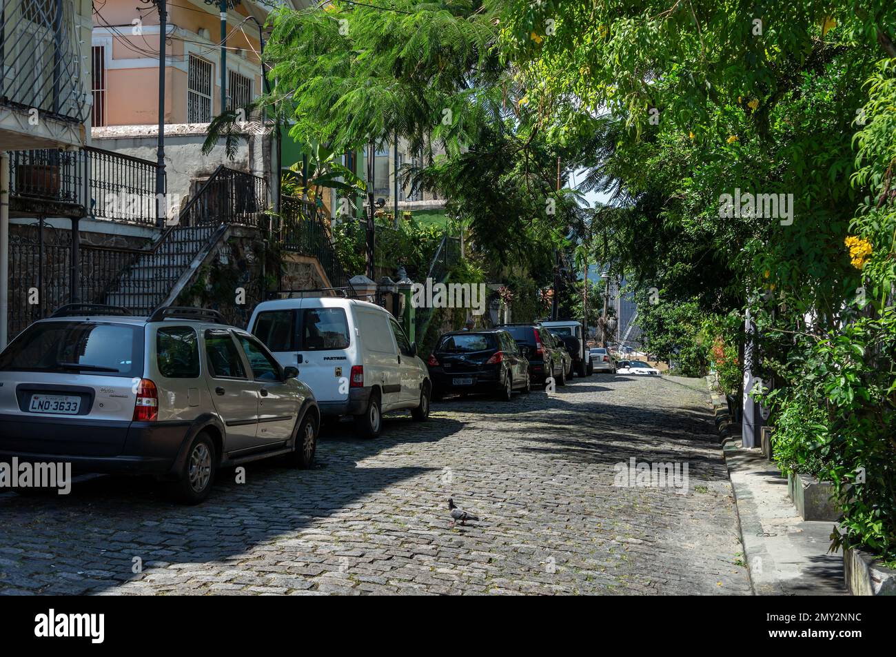 Cars parked on Ladeira de Santa Teresa cobblestone slope street in Santa Teresa district residential area under a summer afternoon sunny blue sky day. Stock Photo