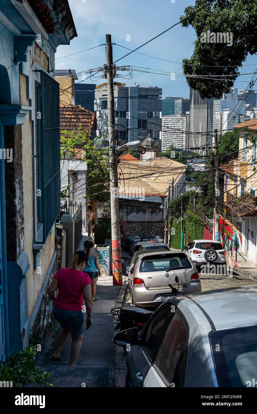 Partial view of Santa Teresa cobblestone slope street with cars parked and Centro district buildings at the back in a summer afternoon sunny blue sky. Stock Photo