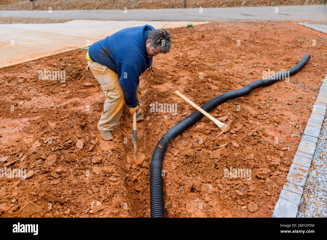 During major rainfall worker digs trench so as to lay drainage pipe for collect rainwater Stock Photo