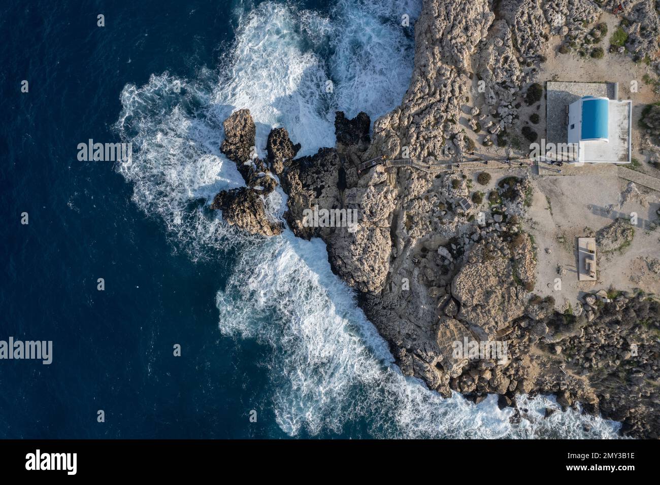 Drone aerial photograph stormy windy waves crashing on a rocky coast . of Cape Greco peninsula with Agioi Anargyroi Christian church Cyprus Europe Stock Photo