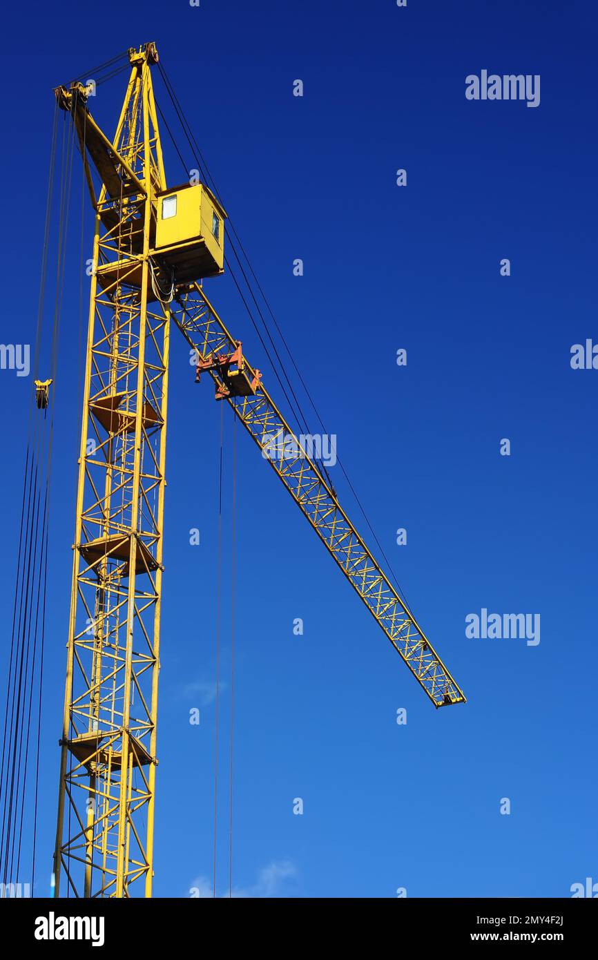 A tall yellow tower crane at a construction site against a blue sky