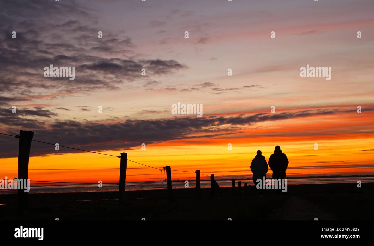 Husum, Germany. 04th Feb, 2023. Two people walk in front of a colorful sky shortly after sunset at the North Sea near Husum. Credit: Christian Charisius/dpa/Alamy Live News Stock Photo