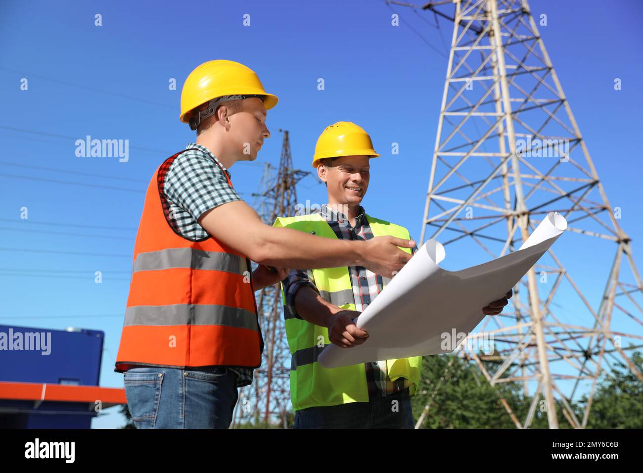 Professional electricians with drafting near high voltage tower Stock