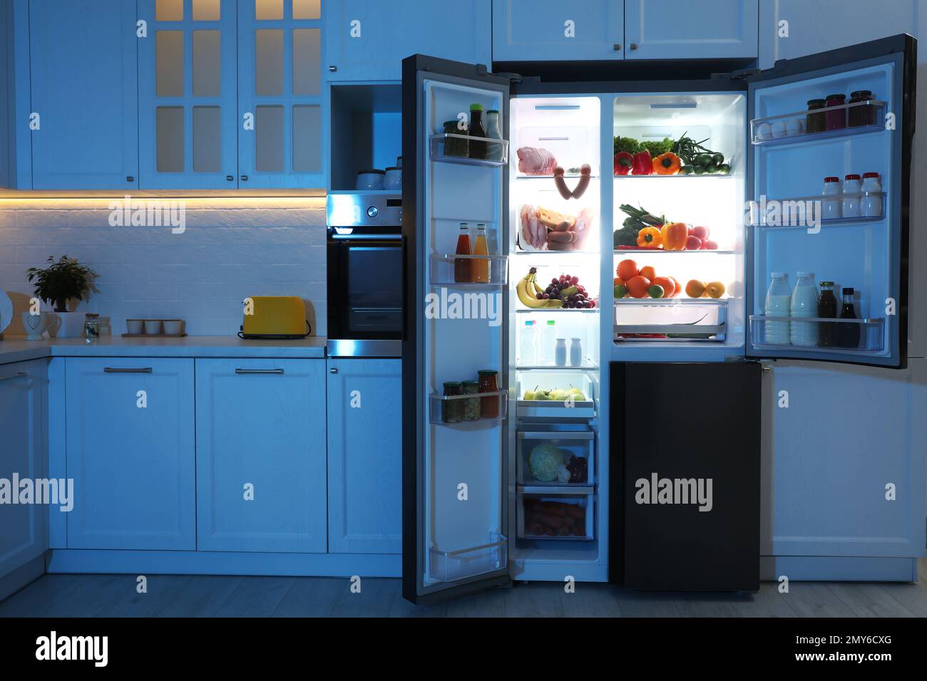 Open refrigerator filled with food in kitchen at night Stock Photo Alamy
