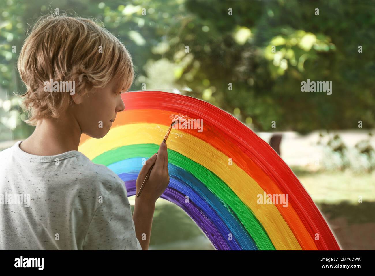 Little boy drawing rainbow on window. Stay at home concept Stock Photo