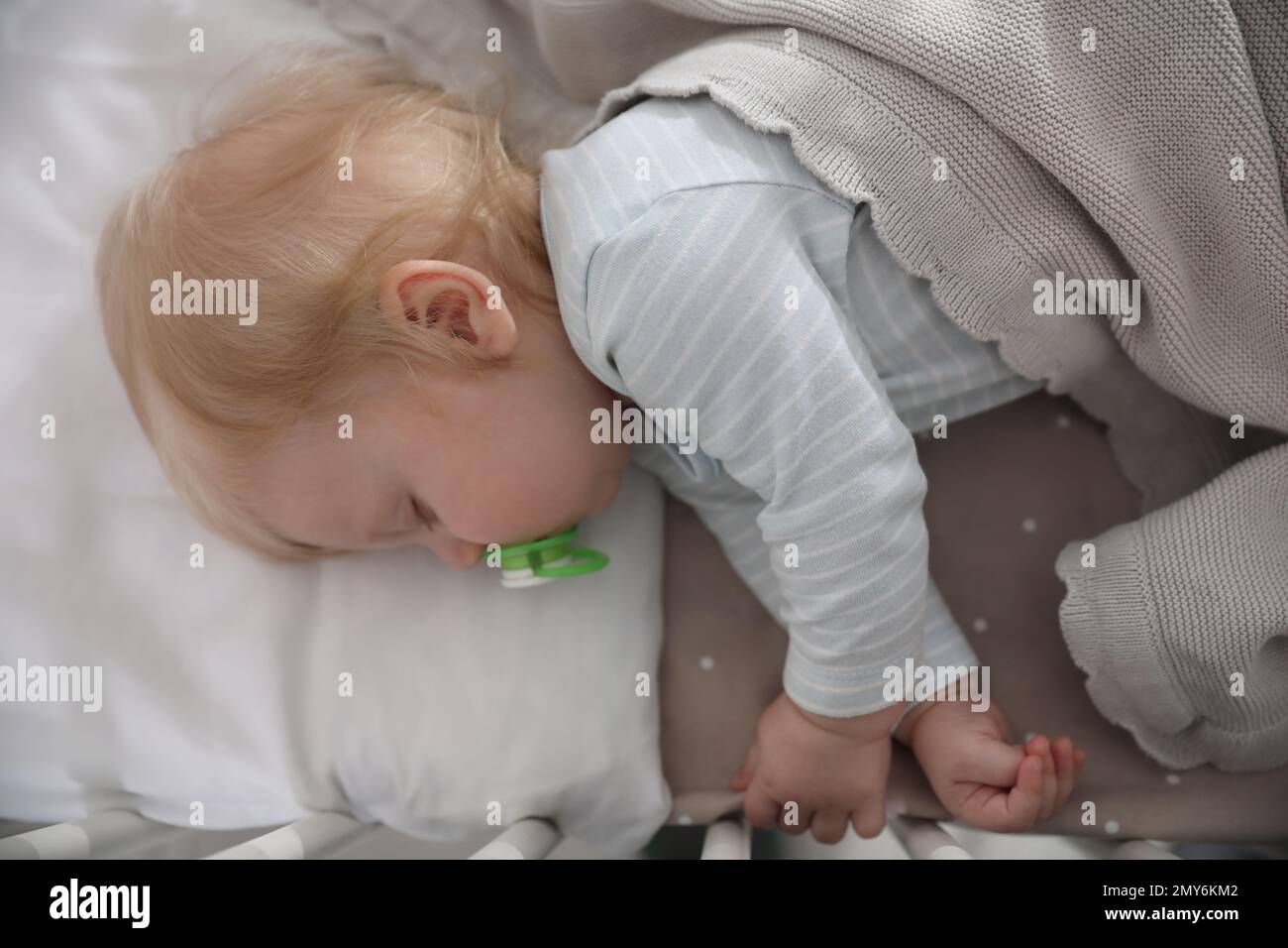 Cute little baby with pacifier sleeping in crib, top view. Bedtime