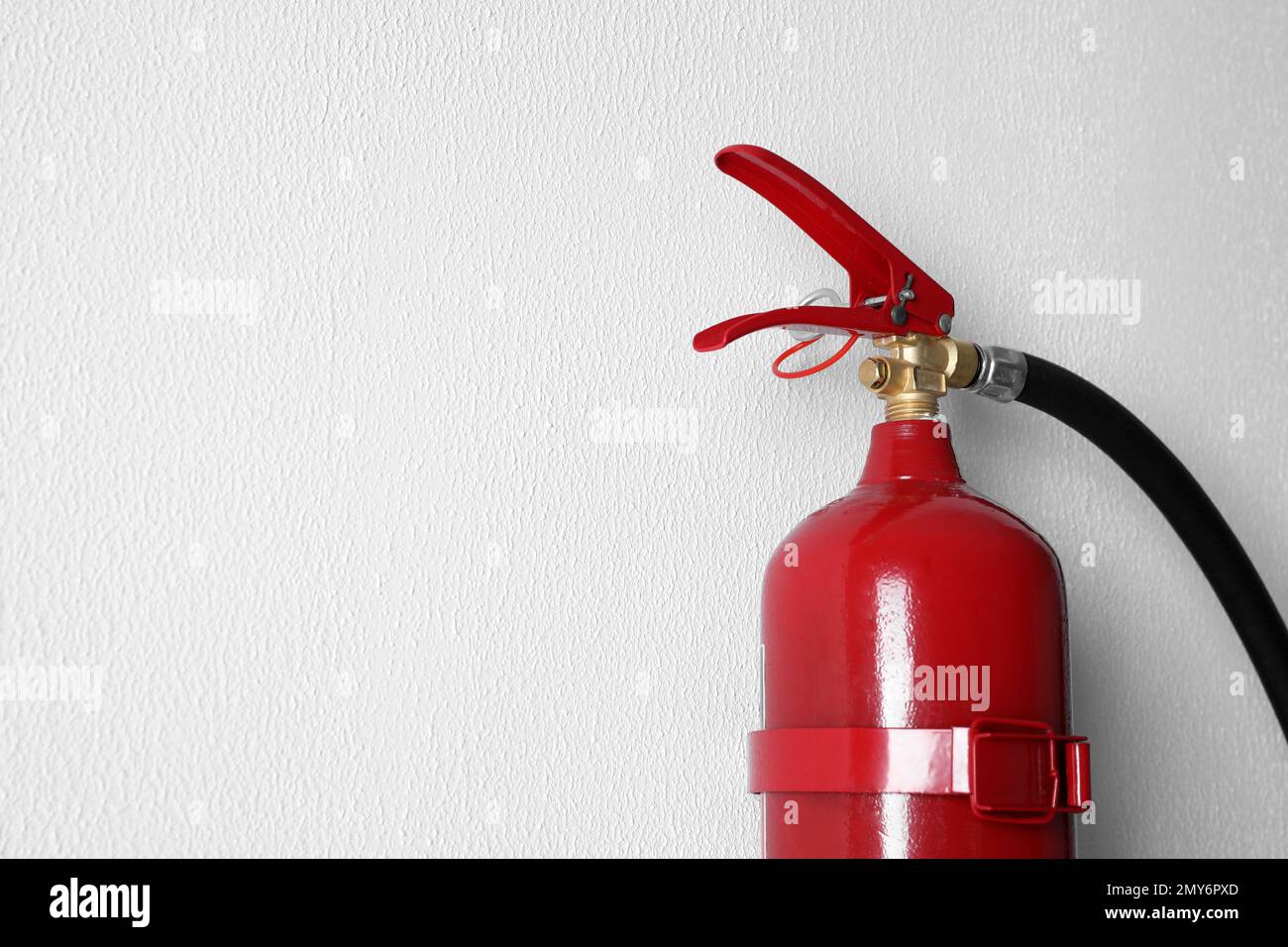Fire extinguisher hanging on white wall, closeup. Space for text Stock