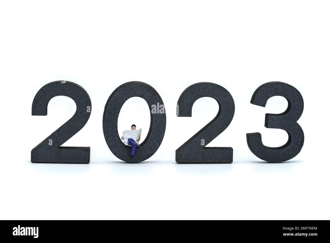2023 Business New Year Concept. Closeup of businessman miniature figures sitting and reading a newspaper on wooden number on white background. Stock Photo