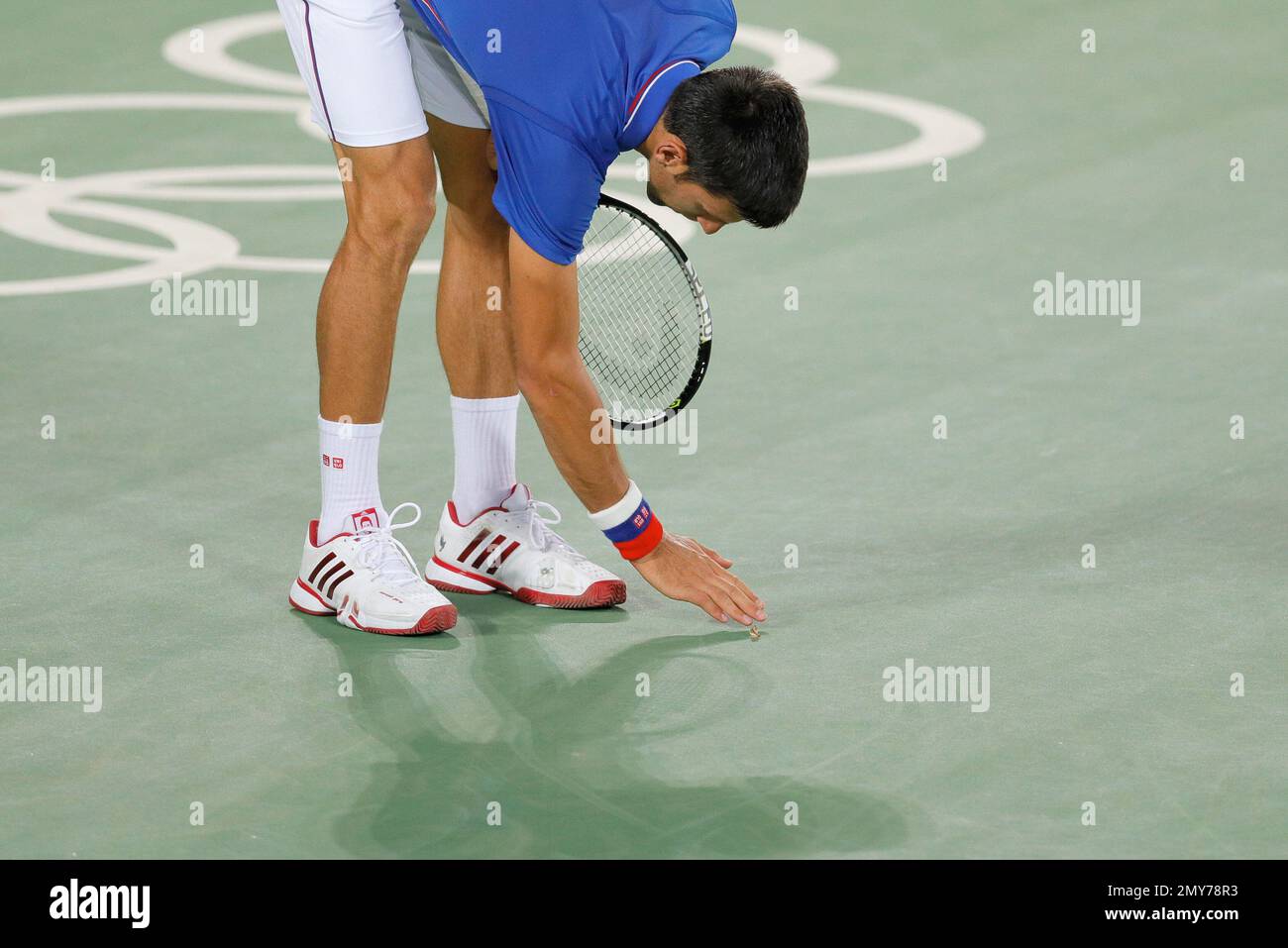 Novak Djokovic, of Serbia, reaches down as he tries to direct a moth away  during his match against Juan Martin del Potro, of Argentina, in the men's  tennis competition at the 2016