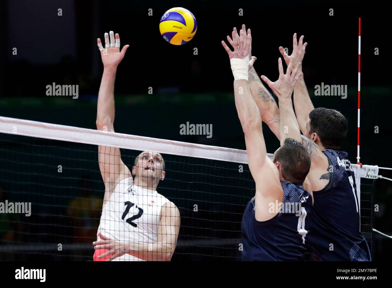 Canada's Gavin Schmitt (12) spikes the ball as United States' David Lee,  center, and Matthew Anderson, right, attempt to block during a men's  preliminary volleyball match at the 2016 Summer Olympics in, image size:1300x956