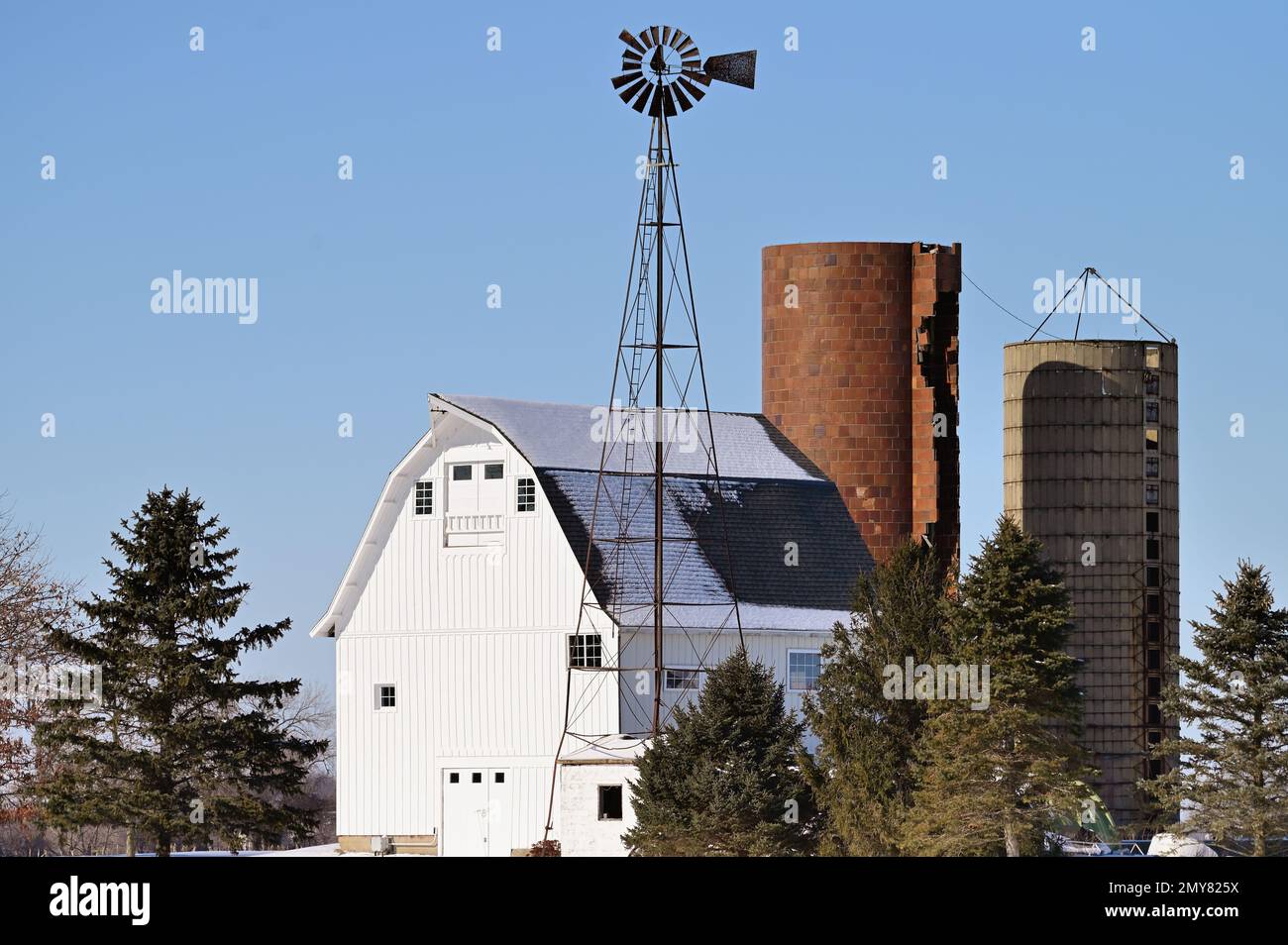 Maple Park, Illinois, USA. A barn along with its silos and windmill stand out from the snow on a bright winter day in northeastern Illinois. Stock Photo