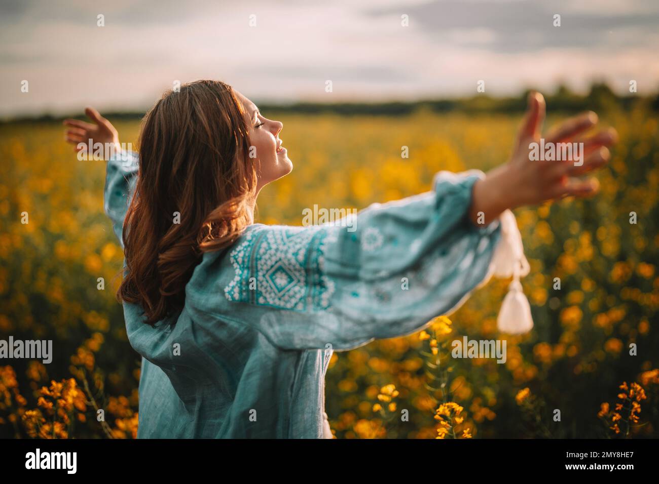 Smiling ukrainian woman standing in yellow canola field. Young lady in blue embroidery vyshyvanka blouse. Ukraine, independence, freedom, patriot symb Stock Photo