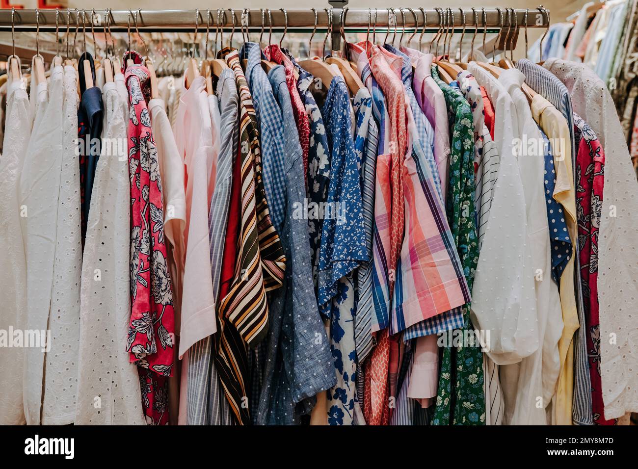 Colorful summer clothes hang on shelf hangers in store. Modern fashion, sale. High quality photo Stock Photo