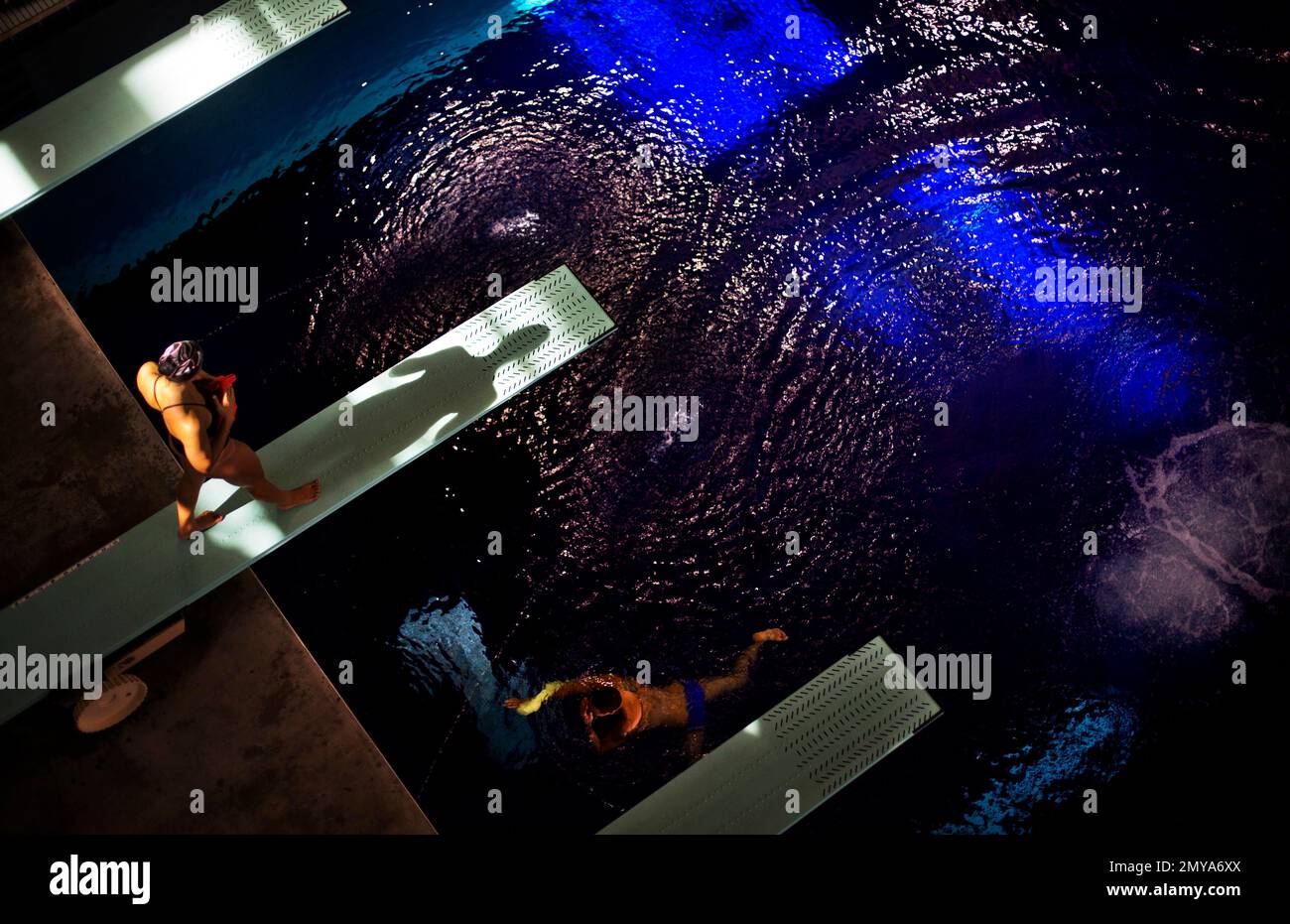A diver casts a shadow on a diving board while practicing at