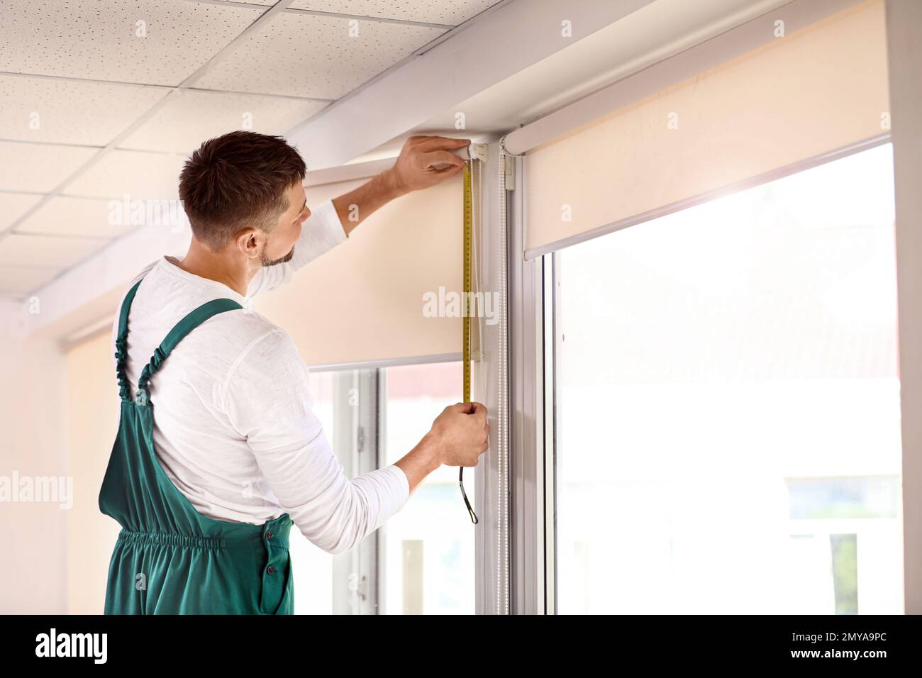 Handyman with tape measure installing roller window blind indoors Stock