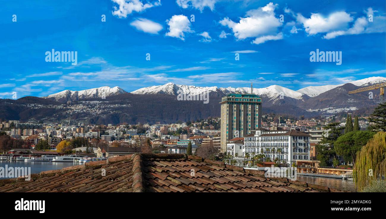 Day winter view on Lugano town and snowcapped mountains behind and forest behind. City Lugano