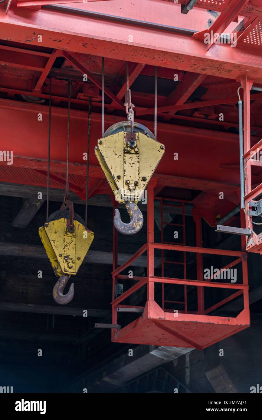 two yellow heavy duty cranes hang by their wire ropes from a red steel