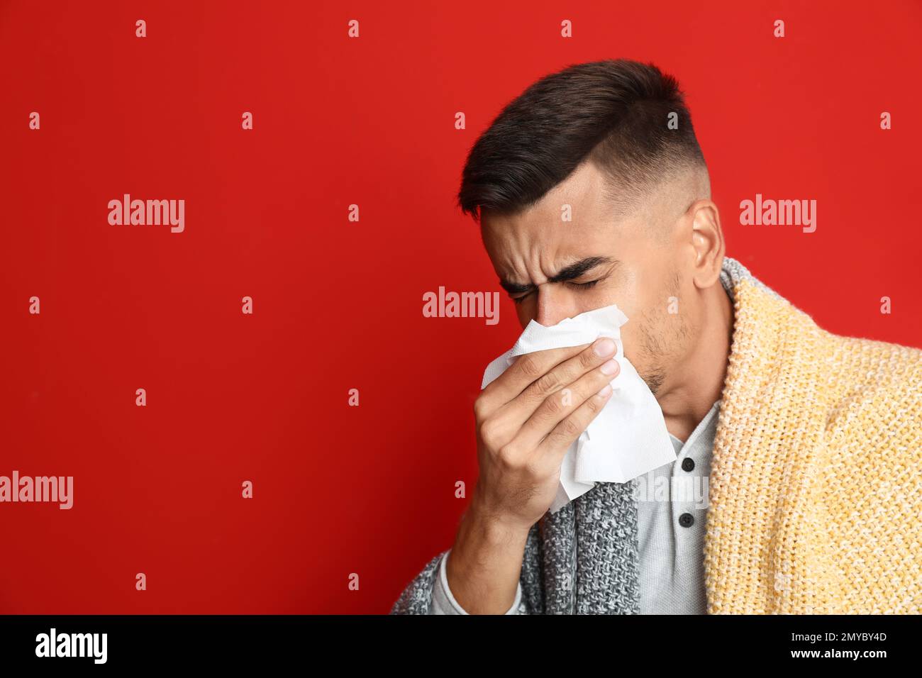 Man sneezing on red background, space for text. Cold symptoms Stock Photo