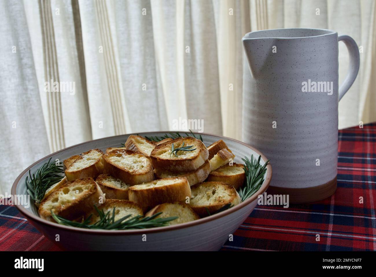 Bowl of toasted bread slices with rosemary and a pitcher Stock Photo
