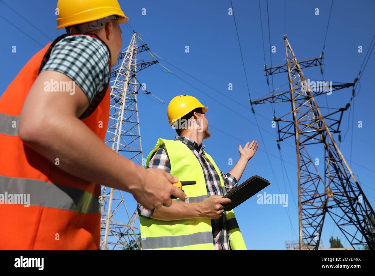 Professional electricians in uniforms near high voltage towers Stock